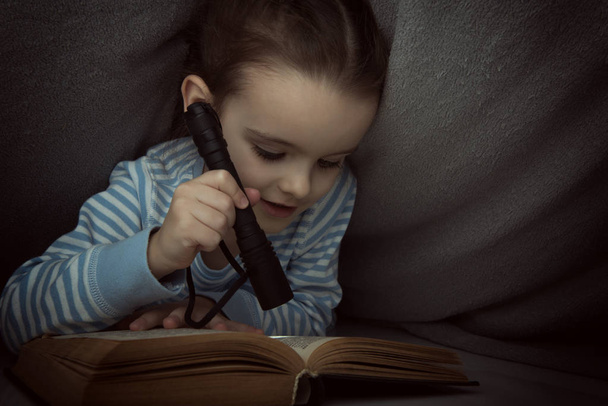 Маленькая девочка читает сказки под одеялом накануне
 - Фото, изображение