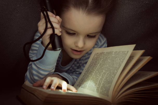 Little girl reading fairy tales book under the covers at the eve - Fotoğraf, Görsel