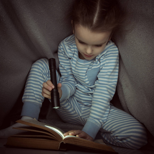Little girl reading fairy tales book under the covers at the eve - Photo, Image