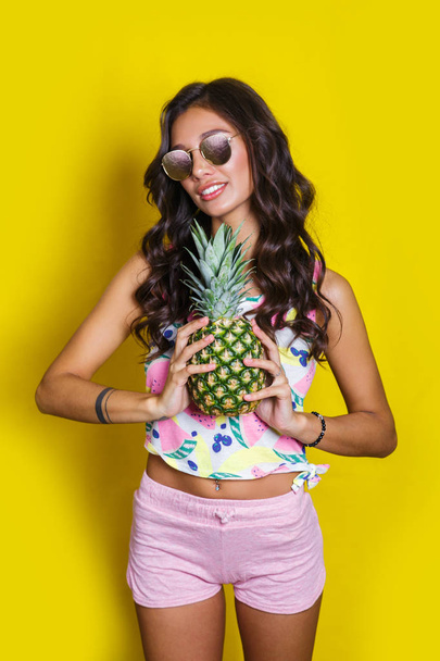 Fashion summer funny portrait indian girl with pineapple over yellow background - 写真・画像