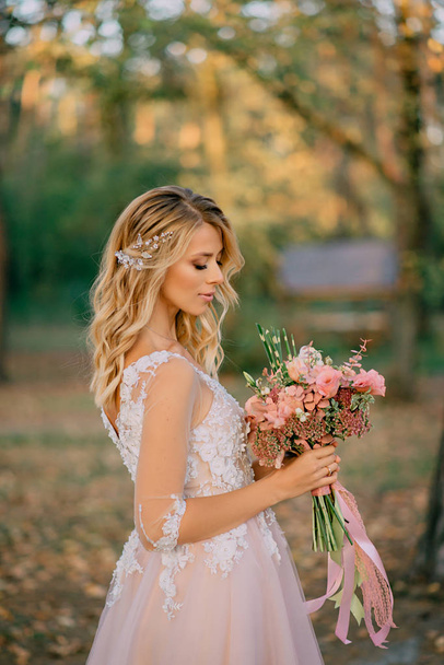 beautiful bride stands with a bouquet in hands on a nature background - Фото, изображение