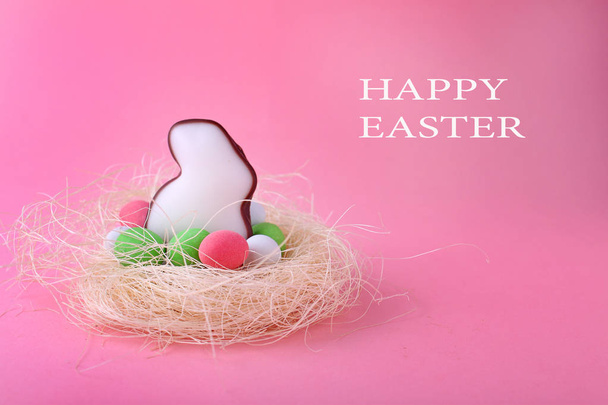 カラフルな卵のピンクの背景に幸せなイースターをレタリングと生気のないクッキーの形をしたウサギの巣します。 - 写真・画像