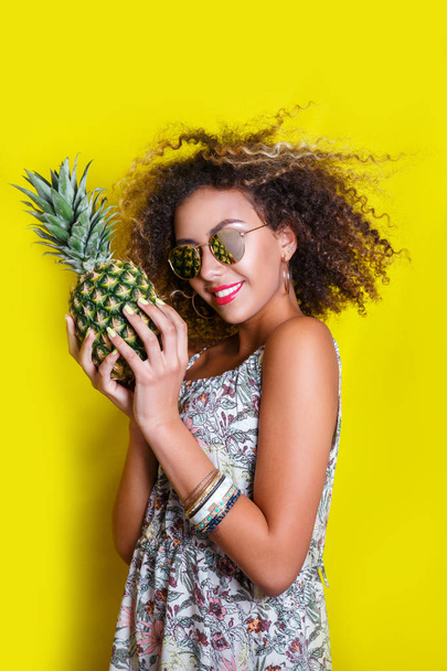 Fashion summer portrait smiling afro american girl in sunglasses and pineapple over yellow background - Fotoğraf, Görsel