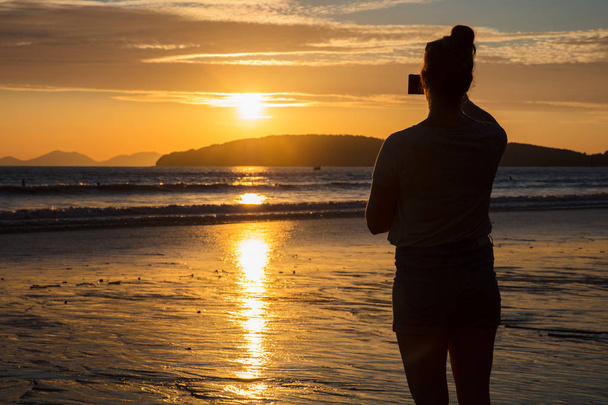 Silueta mujer fotografiando puesta de sol en la playa
 - Foto, imagen