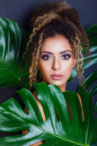 Close-up Portrait of an African American Black Woman with evening make-up and tropical leaves on black background - Fotografie, Obrázek