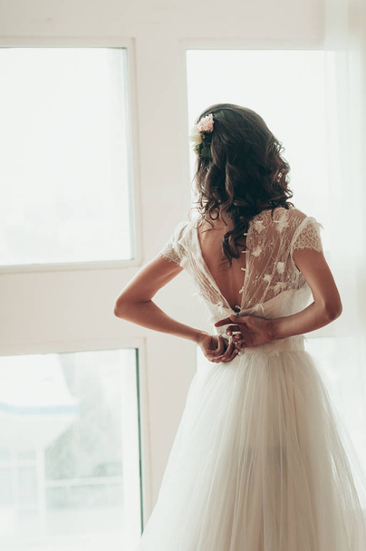 A bride buttoning her dress next to a window, a view from her ba - Foto, Imagen