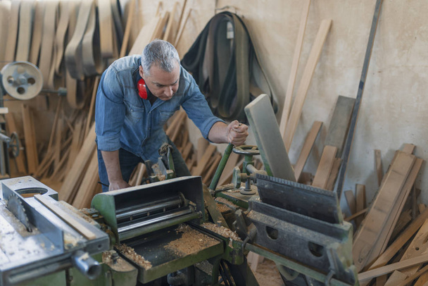 Timmerman werkt aan houtbewerkingsmachines in timmermanswerkplaats. - Foto, afbeelding