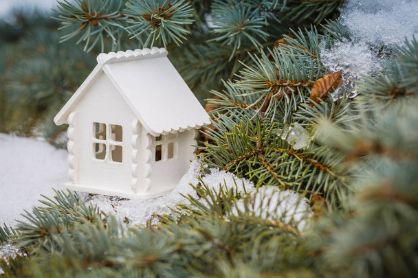 Juguete casa blanca está en la rama de pino con nieve
 - Foto, imagen