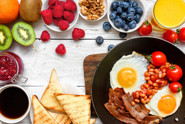 Angol reggeli - sült tojás, bab, paradicsom, kávé, szalonna és pirítóssal, friss gyümölcsök és bogyók - Fotó, kép