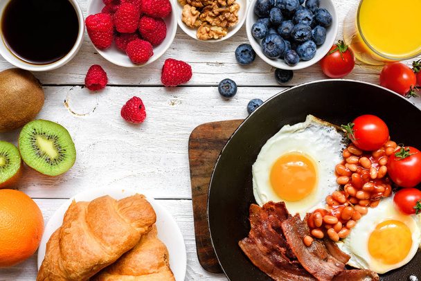 Desayuno con café, huevo frito, tocino, frijoles, croissant, zumo de naranja con frutas y bayas
 - Foto, Imagen