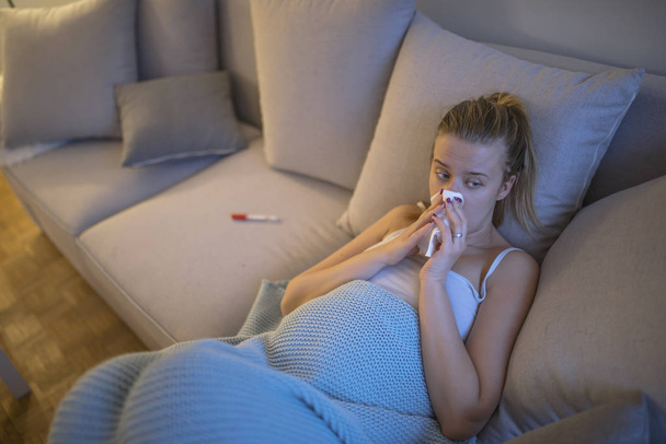Upset young pregnant woman suffering from influenza with handkerchief on sofa at home - Foto, afbeelding