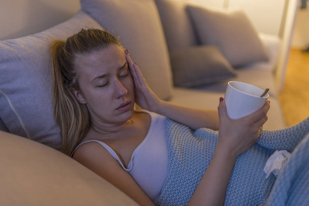 Upset young woman suffering from influenza at home and drinking tea during fever.  - Foto, afbeelding
