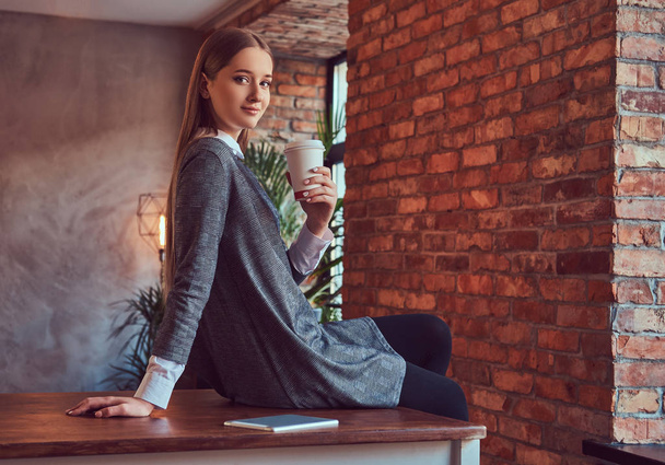 Slim αισθησιακή κοπέλα με ένα γκρι φόρεμα κατέχει ένα φλυτζάνι του καφέ  - Φωτογραφία, εικόνα