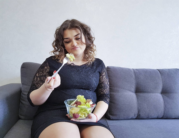 mooi full-length meisje zittend op de Bank met een plaat van salade - Foto, afbeelding