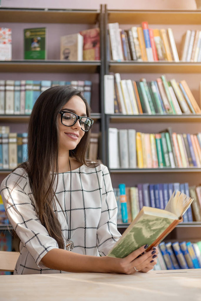 Jonge mooie brunette is het lezen van een boek in de bibliotheek. - Foto, afbeelding