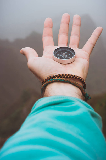 Hand with compass on the rock in front of the monumental mountain range silhouette in the fog - Fotografie, Obrázek