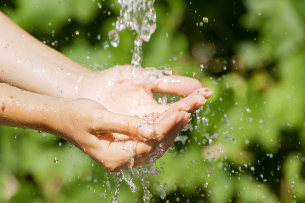 Vrouw wassen hand buitenshuis. Natuurlijke drinkwater in de palm. Jonge handen met water splash, selectieve aandacht - Foto, afbeelding
