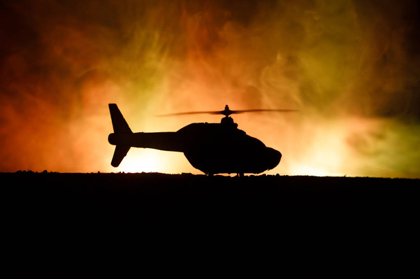 Silhouette of military helicopter ready to fly from conflict zone. Decorated night footage with helicopter starting in desert with foggy toned backlit. Selective focus. - Fotografie, Obrázek