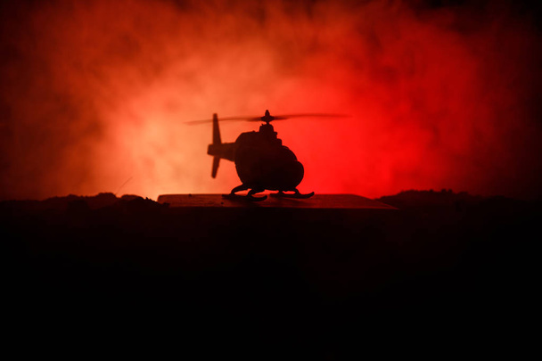 Silhouette of military helicopter ready to fly from conflict zone. Decorated night footage with helicopter starting in desert with foggy toned backlit. Selective focus. - Photo, Image