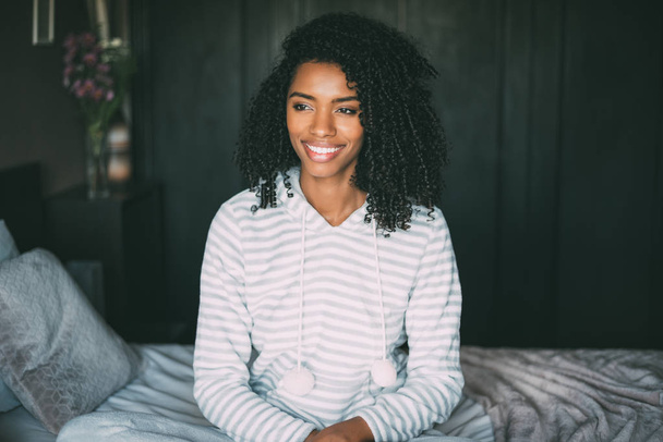 primer plano de una bonita mujer negra con el pelo rizado sonriendo y acostada en la cama mirando hacia otro lado
 - Foto, imagen