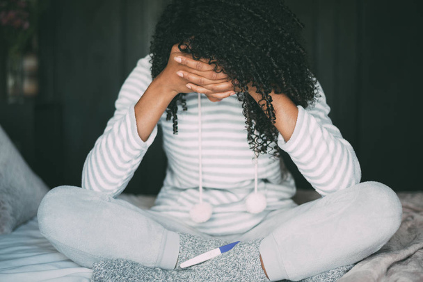 вдумлива хвилююча і сумна чорна жінка з тестом на вагітність в ліжку
 - Фото, зображення