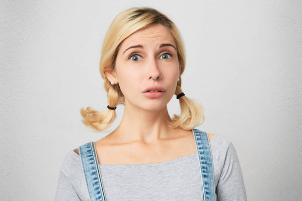Portrait of young blonde girl feels uncertain, wears overalls. Female feels confused about new rules in high school.  - Photo, Image