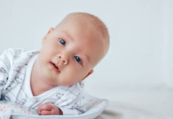 Un bébé drôle avec de beaux yeux repose sur son ventre et sourit
. - Photo, image