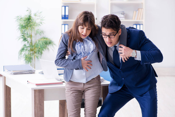 Pregnant woman struggling in the office and getting colleague he - Photo, Image