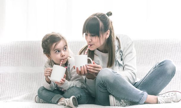 Äiti ja tytär juovat teetä sohvalla
 - Valokuva, kuva