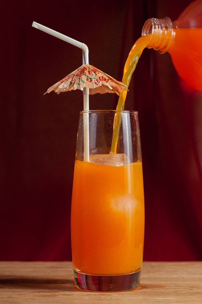 jet pours Orange Drink with ice and umbrella against red background - Photo, Image