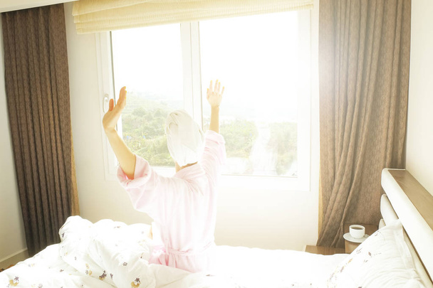 großes, geräumiges Hotelzimmer voller Sonnenlicht und Sonnenstrahlen. optimistischer Start in den Tag. Blonde Frau gemütliche Kleidung zu Hause begrüßt den Morgen Tageslicht. neuer Tag neues Ich-Konzept. - Foto, Bild