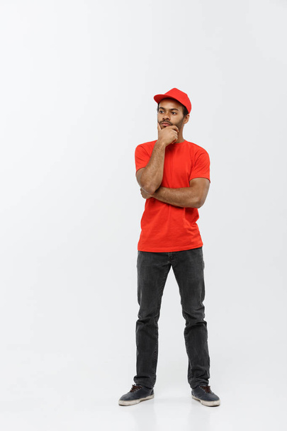 Delivery Concept - Un bell'uomo di consegna afroamericano che pensa seriamente a qualcosa. Isolato su sfondo grigio studio. Copia spazio
. - Foto, immagini
