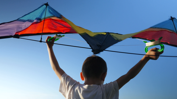 Rückseite kleiner Junge weißes Hemd über seinem Kopf angehoben Drachen auf Hintergrund blauer Himmel - Filmmaterial, Video
