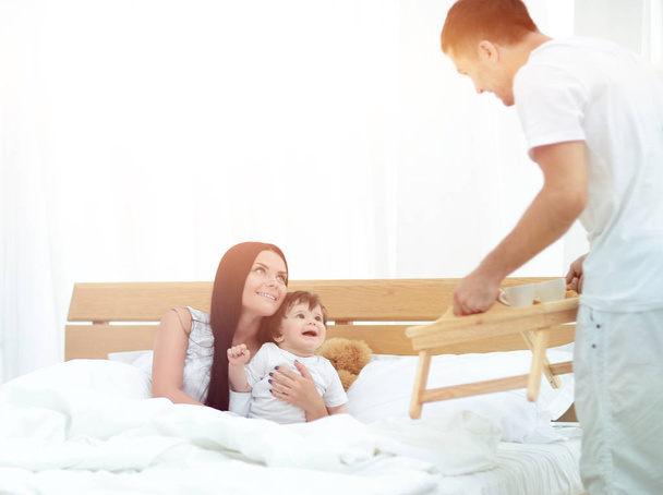 Family with little baby having breakfast in the bed. - Photo, image