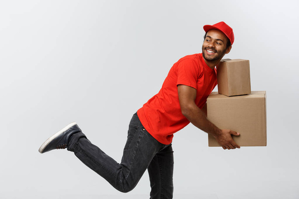 Teslimat kavramı - müşteri için bir paketi teslim etmek için çalışan yakışıklı Afro-Amerikan teslimat adam acele. Arka plan gri studio izole. Kopya alanı. - Fotoğraf, Görsel