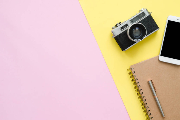 Flat lay design of travel summer concept - Top view of brown notebook, pencil, tablet and camera on pink and yellow pastel color screen with a copy space. travel summer on pastel color background. - Photo, Image
