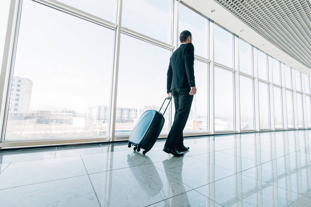 Młody biznesmen ciągnięcie walizkę w nowoczesne Lotnisko terminal. Podróży facet lub biznesmen koncepcja. Podróż służbowa - Zdjęcie, obraz