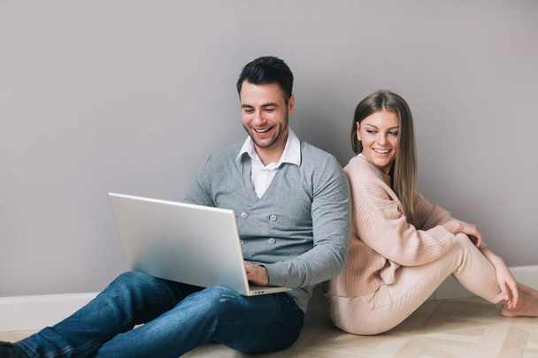 Couple with laptop smiling sitting on the floor. - Photo, image
