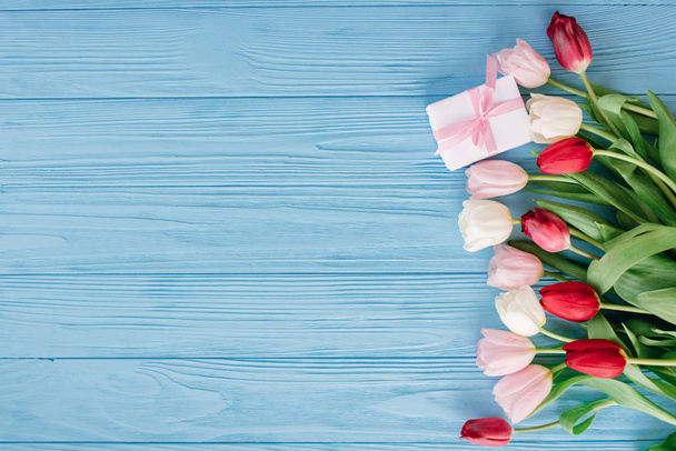 Composición floral de tulipanes coloridos colocados en fila en el lado derecho sobre fondo de madera azul con caja de regalo
 - Foto, imagen