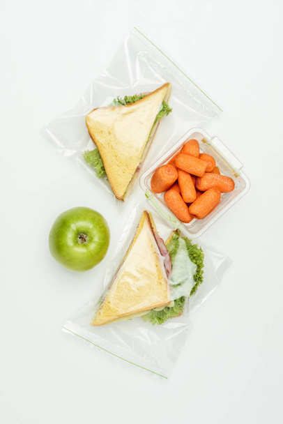 top view of sandwiches in ziplock bags and carrots in lunch box isolated on white - Фото, изображение