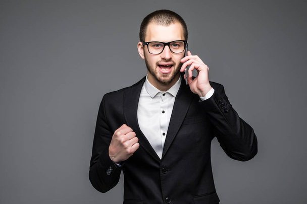 Onnellinen liikemies puhuu puhelimessa ja juhlii menestystään harmaalla taustalla
 - Valokuva, kuva