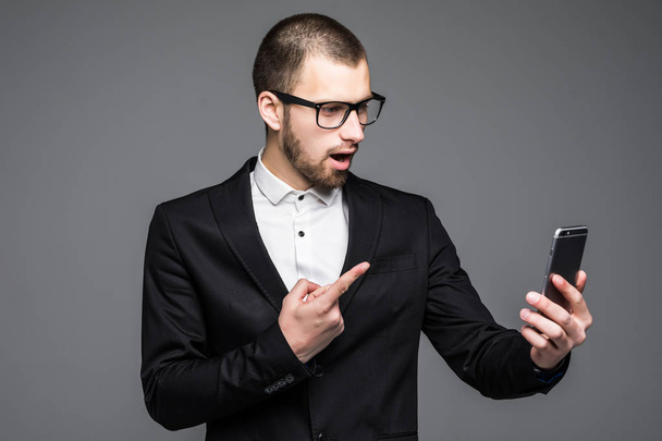zufriedener Geschäftsmann zeigt mit dem Finger auf Smartphone-Bildschirm über grauem Hintergrund. - Foto, Bild