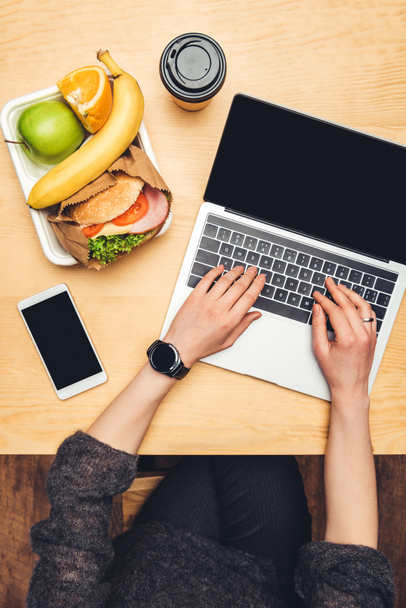 imagem cortada da mulher usando laptop à mesa com alimentos no recipiente
 - Foto, Imagem