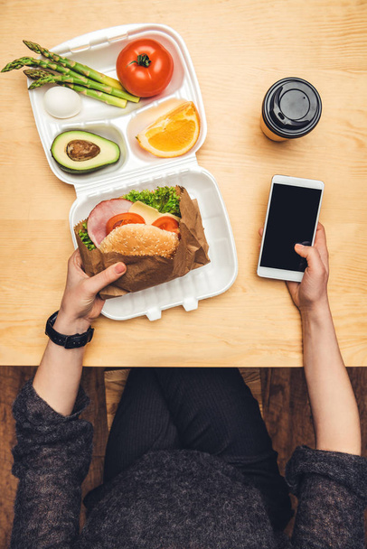 immagine ritagliata di donna che tiene hamburger e smartphone in mano
 - Foto, immagini