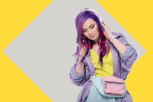 стильна молода жінка з барвистим волоссям у фіолетовому траншеї пальто слухає музику з навушниками
 - Фото, зображення