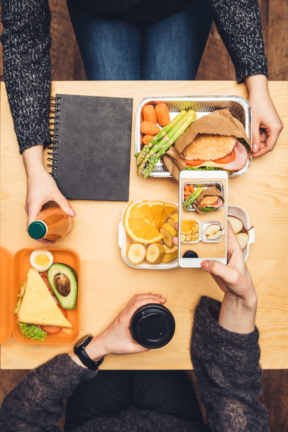 imagen recortada de la mujer sentada en la mesa y tomando una foto del almuerzo con el teléfono inteligente
 - Foto, Imagen