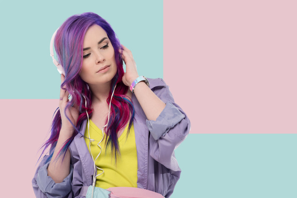 beautiful young woman with colorful hair in purple trench coat listening music with headphones - Photo, Image