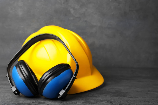 Headphones and hard hat on table against grey background. Hearing protection equipment - Foto, Imagem