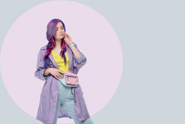 hermosa mujer joven en gabardina púrpura escuchando música con auriculares en un fondo creativo
 - Foto, Imagen