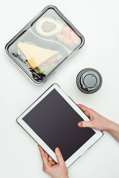 image recadrée d'une femme tenant un comprimé à table avec de la nourriture dans une boîte à lunch isolée sur blanc
 - Photo, image